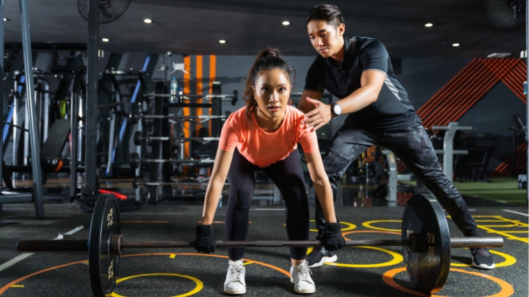 A person working out with a barbell and being coached.