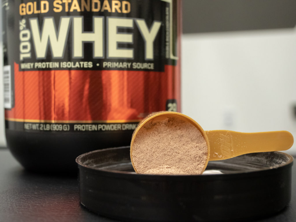 A scoop of Optimum Nutrition Gold Standard rest on the lid of the container.