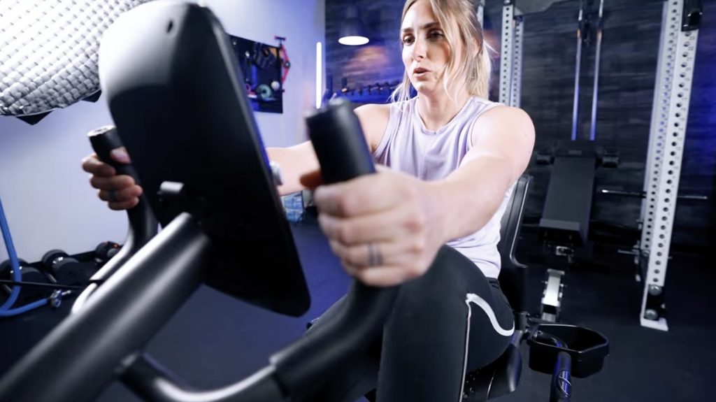 A BarBend tester is shown holding the handles while riding a Schwinn Recumbent exercise bike.