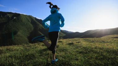 A person wearing athletic gear, and a jacket, trail running in the mountains.