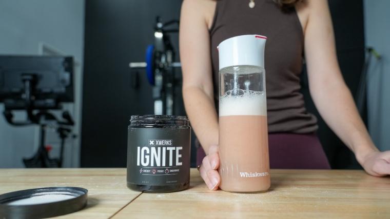 A shaker glass of XWERKS Ignite next to the container